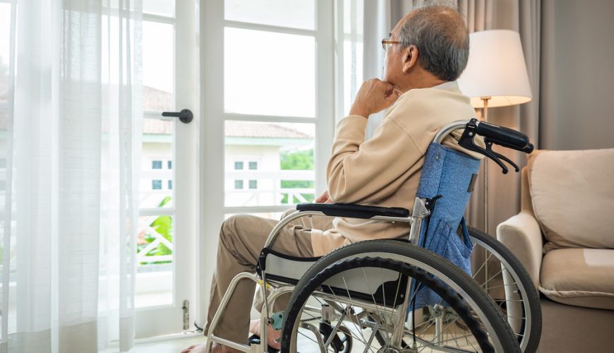 Adulto mayor sentado en silla de ruedas viendo por una ventana